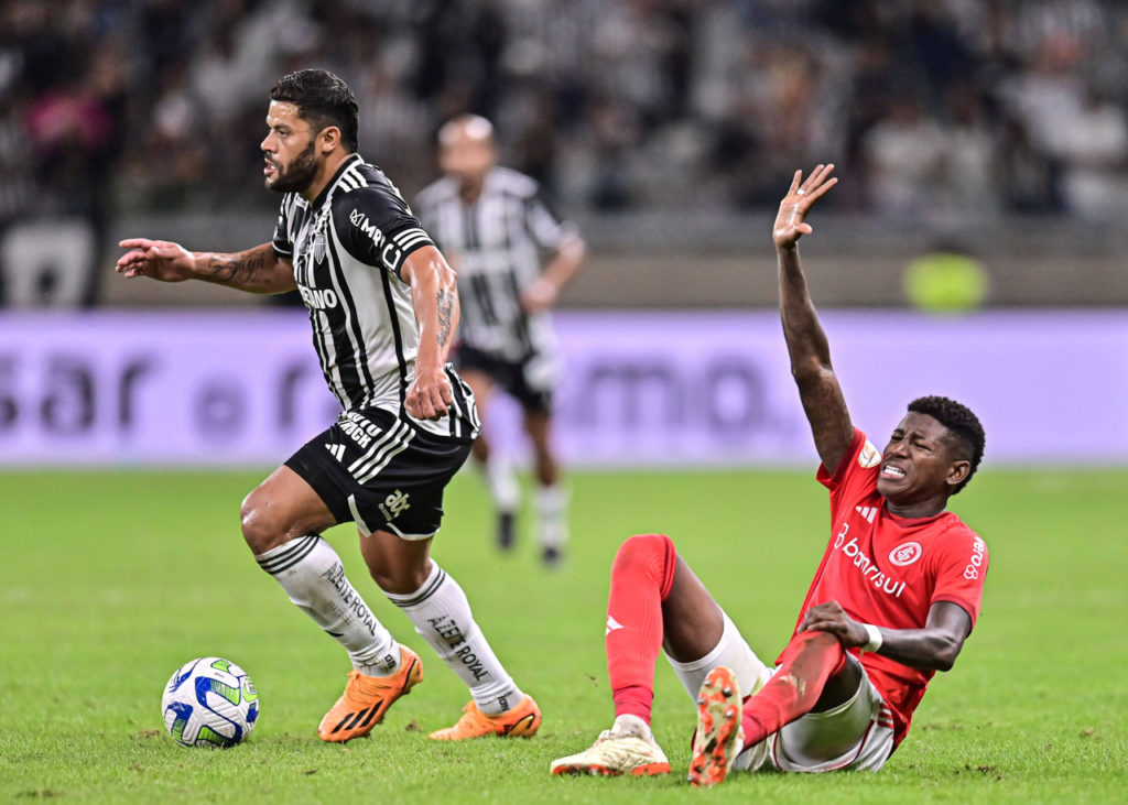 Vitão, zagueiro do Internacional, sentado no gramado com a mão levantada durante uma partida de seu clube.