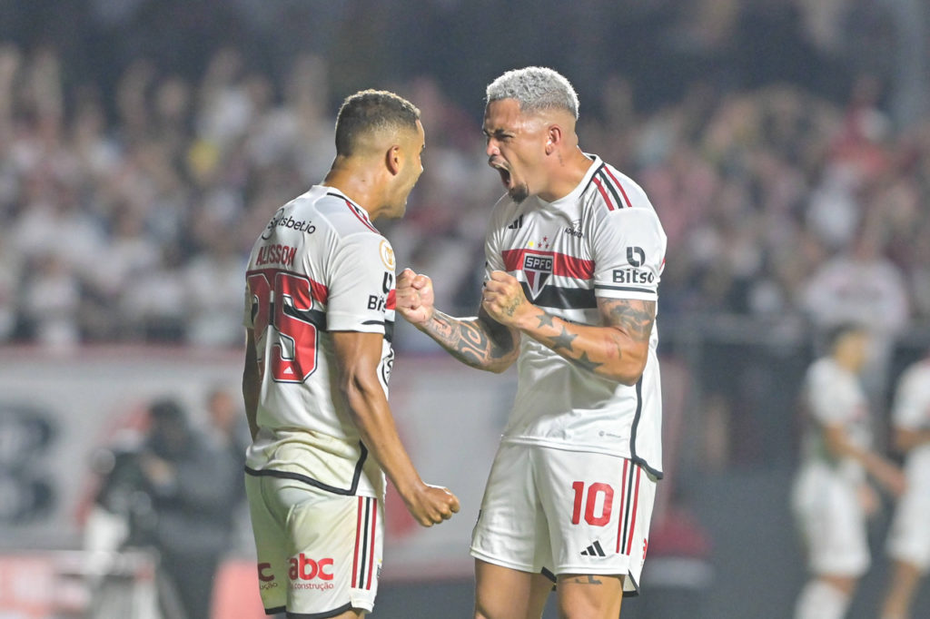 Luciano e Alisson, jogadores do São Paulo, comemoram um gol com a camisa do time durante uma partida.