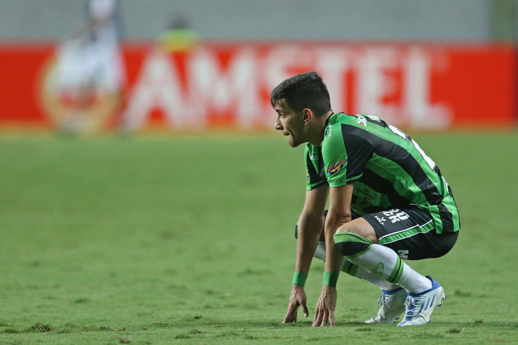 Pedrinho, atacante, fica agachado no gramado durante uma partida de quando o o jogador ainda atuava pelo América-MG.