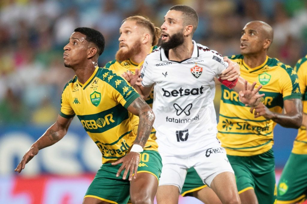 Jogadores de Cuiabá e Vitória observam a bola em uma jogada durante o confronto entre as equipes.