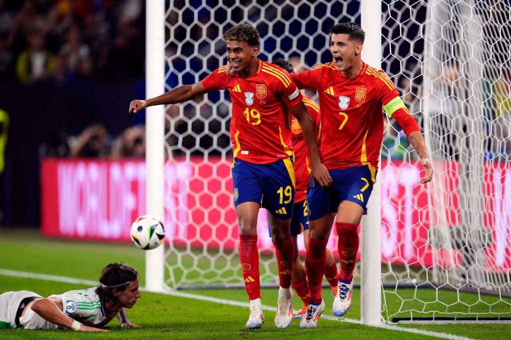 Calafiori cai no gramado após fazer gol contra na derrota da Itália para a Espanha, enquanto Lamine Yamal e Morata comemoram para a Espanha